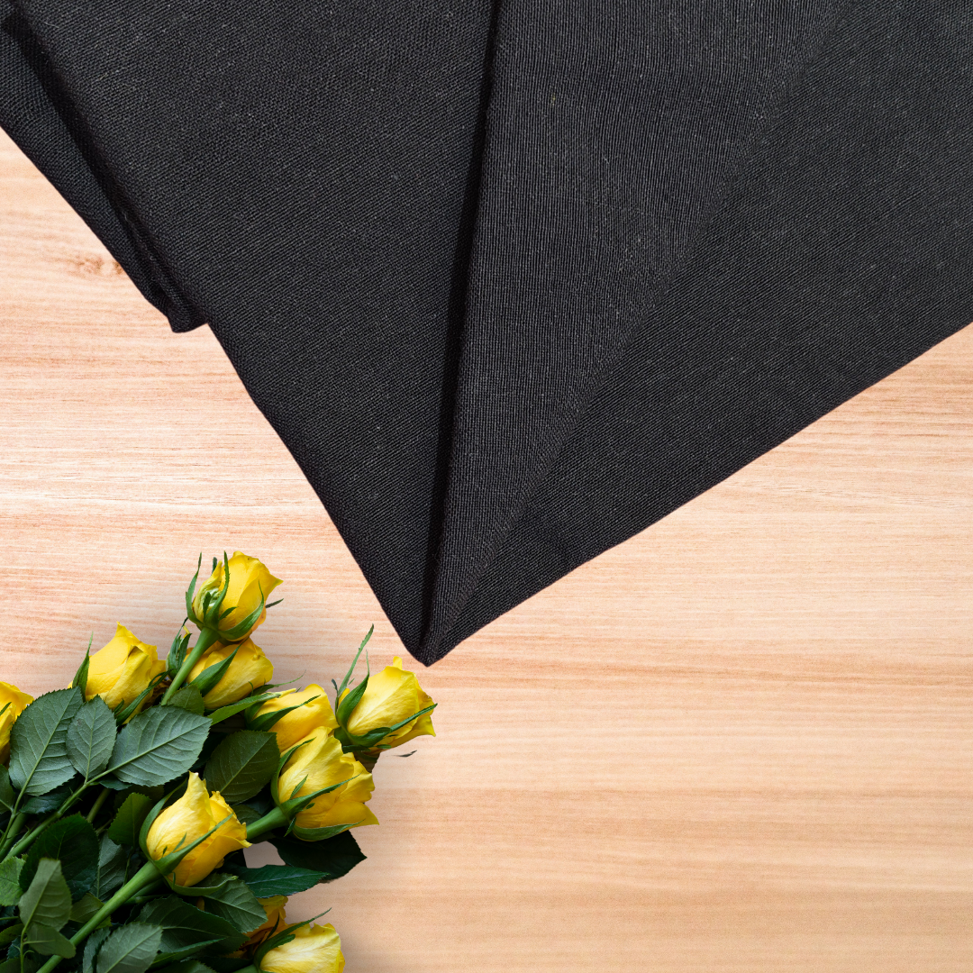 top view of the classic black casement embroidery fabric in teal placed on a light brown wooden table with yellow rose bunch and green leaves
