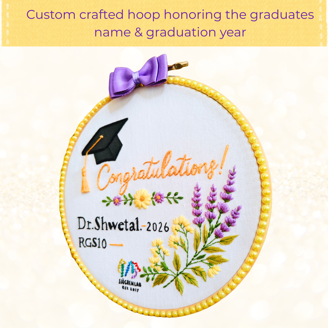 A circular embroidery hoop with a yellow beaded edge and a purple ribbon bow, featuring a graduation-themed design with a black mortarboard cap, orange 'Congratulations!' script, personalized text, and embroidered flowers on white fabric.