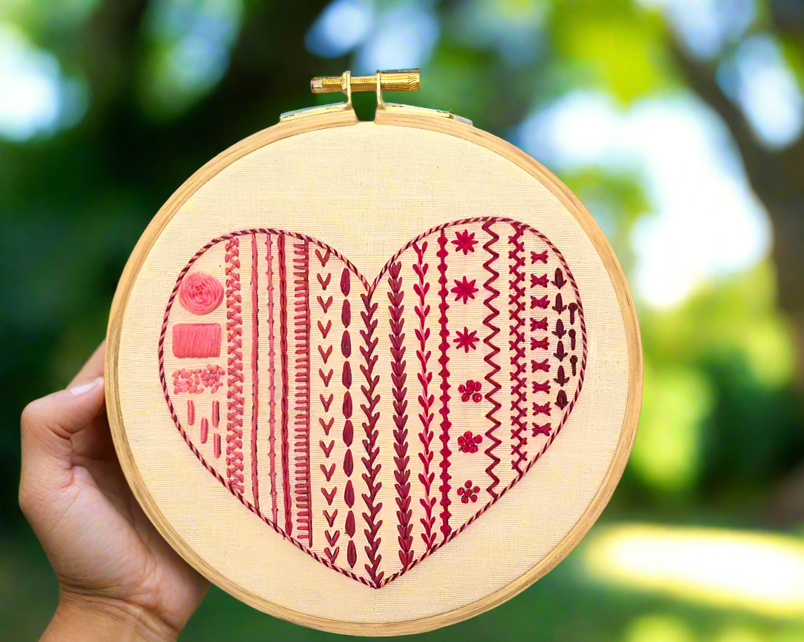 Embroidery hoop art with heart shape design, multiple stitches. modern embroidery pattern in different shades of red thread