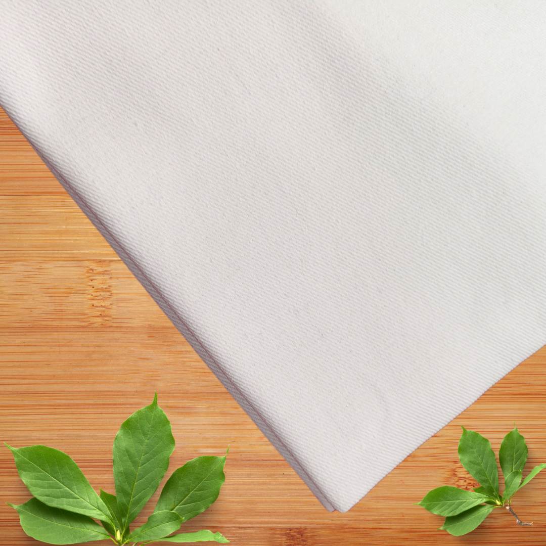 White color fabric with diagonal weave that is most suited for fine needlework, placed on walnut wooden table, from top view with large leaf bunch placed near the left corner and small leaf bunch placed on the right corner, creating a nature inspired super creative concept.
