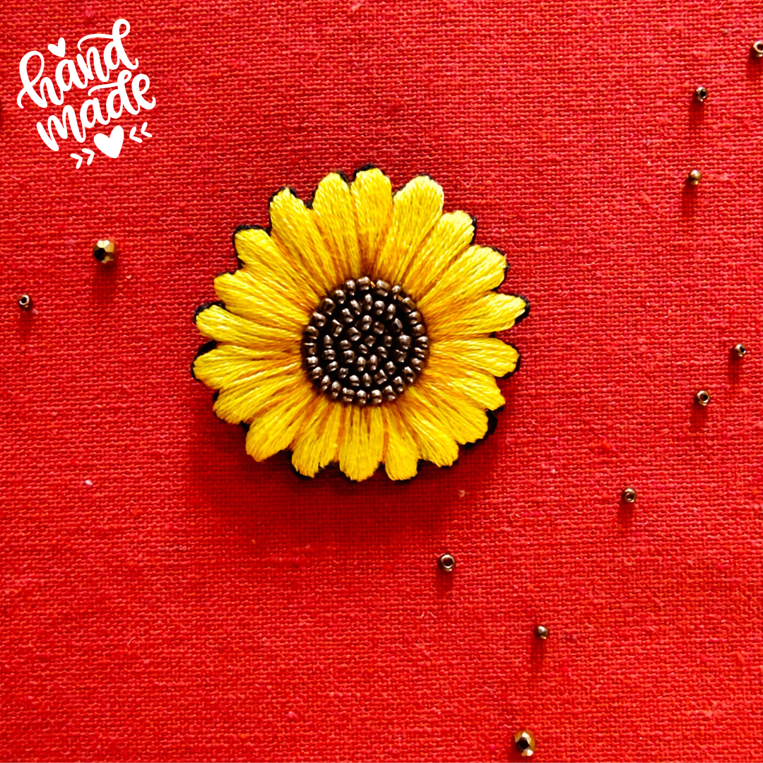 Beautiful sunflower brooch with metallic golden brown shiny beads decorated in the center, place on a bright red fabric with shiny beads scattered here and there