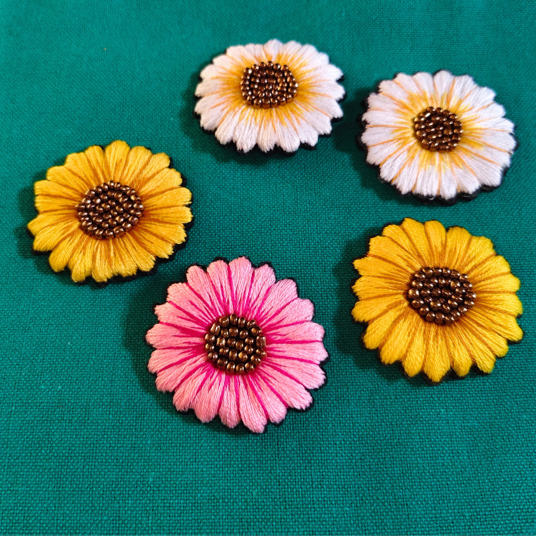 creative flower bunch embroidery brooches with two yellow flowers, two white flowers and one pink flower arranged on a green colored fabric