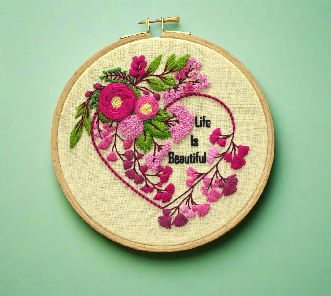 beautiful embroidery hoop with pink floral heart shape embroidery design, green leaves, pink buds and life is beautiful lettering, spiring flowers theme embroidery pattern