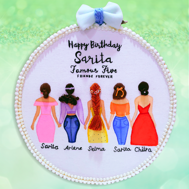 A personalized round embroidered hanging plaque with a white pearl-beaded border and a white bow at the top. The center reads 'Happy Birthday Sarita Famous Five FRIENDS FOREVER' above illustrated women in pink, blue, yellow, orange, and red dresses, with names written below each figure.