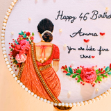 Close up image of embroidered lady's backside view holding pink color flower bouquet, pearl decorations to the hoop border, with happy birthday amma embroidered letters and little hearts