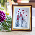 a rectangular, photo of couple with embroidered all over red hearts and red garland with white dots and golden tassels on the garland, framed in a brown and golden wooden frame